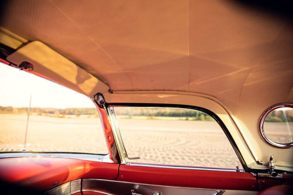 Vintage car interior, red and beige, overlooking sandy expanse.