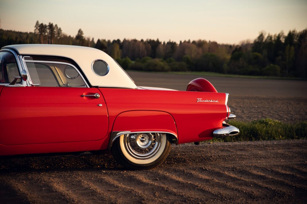 Red vintage Thunderbird car on countryside road at sunset.