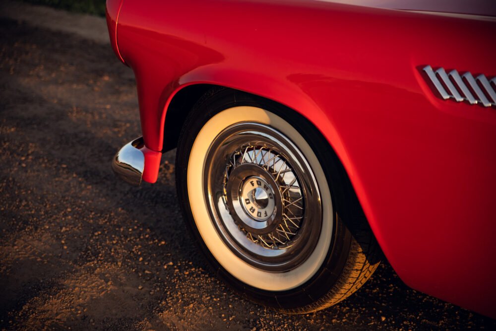 Red vintage car with chrome wire wheel at sunset.