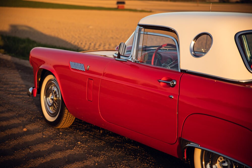 Vintage red and white convertible car at sunset.