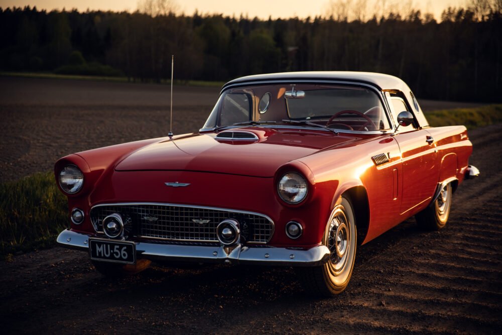 Vintage red Ford Thunderbird parked in countryside at sunset.