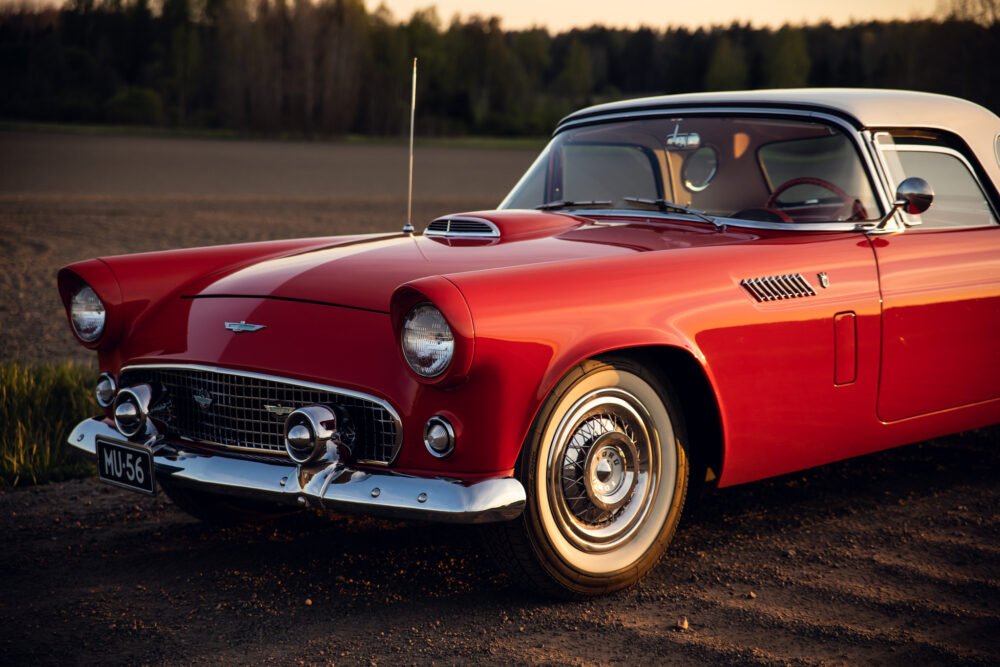 Vintage red Ford Thunderbird on rural road at sunset.