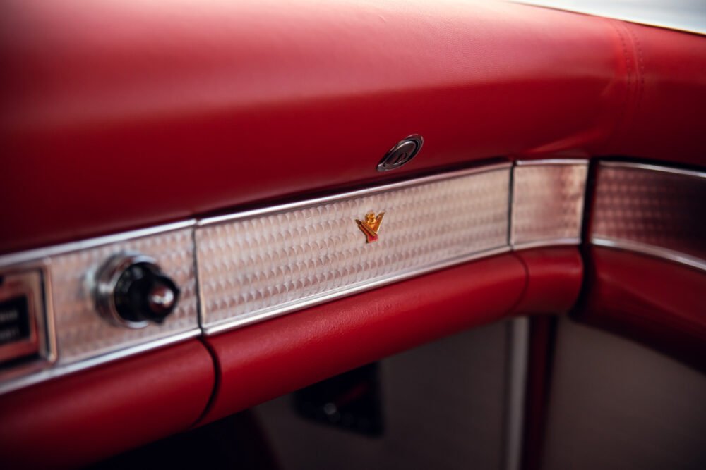 Close-up of vintage car's red dashboard with emblem.
