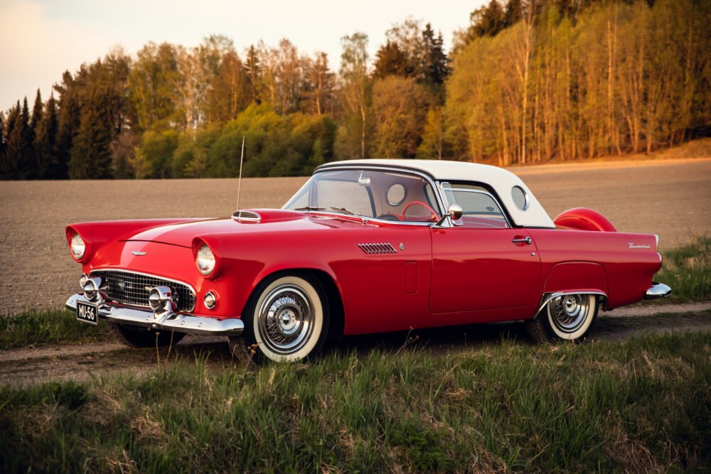 Classic red Thunderbird car parked in countryside at sunset.