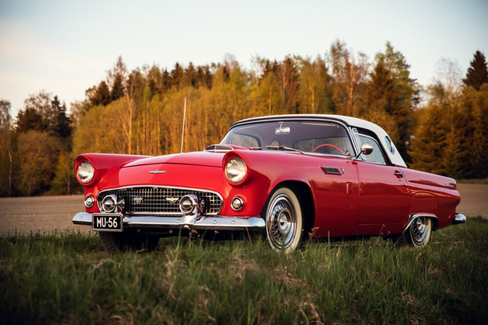 Vintage red convertible car in forest at sunset.