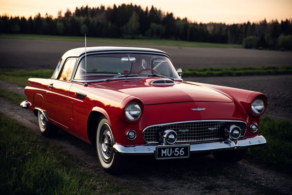 Classic red 1956 Ford Thunderbird parked in rural setting.