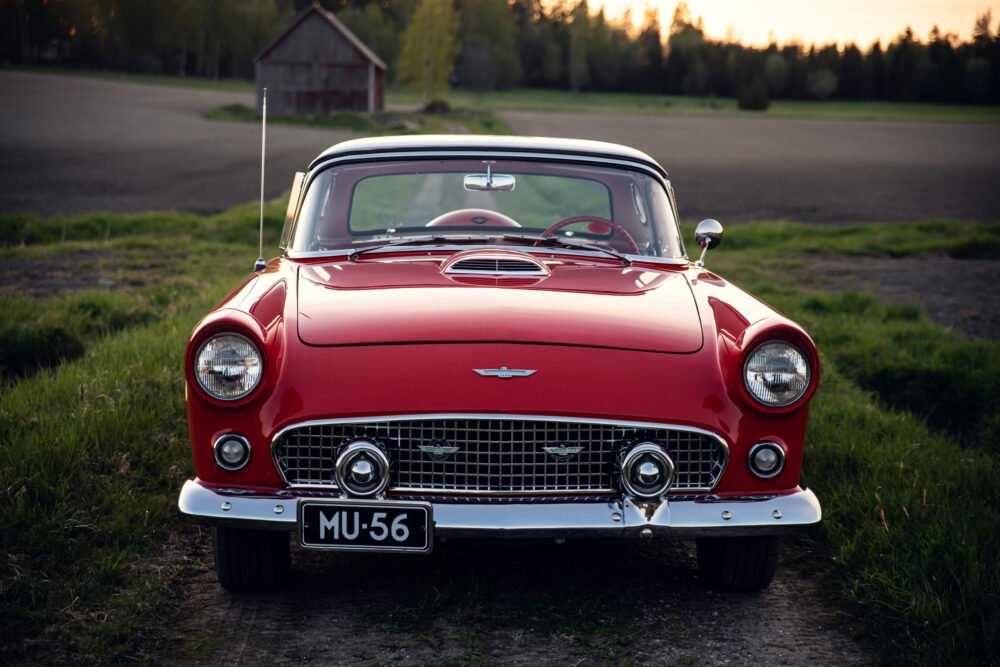 Vintage red Ford Thunderbird on rural road at dusk.
