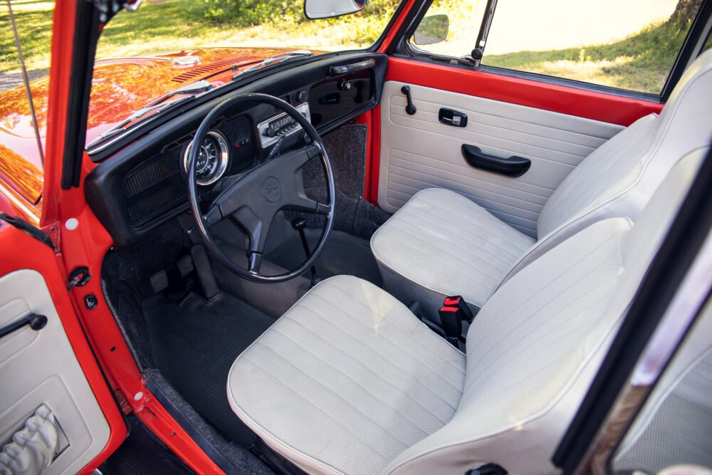 Vintage red car interior, white seats, dashboard view.