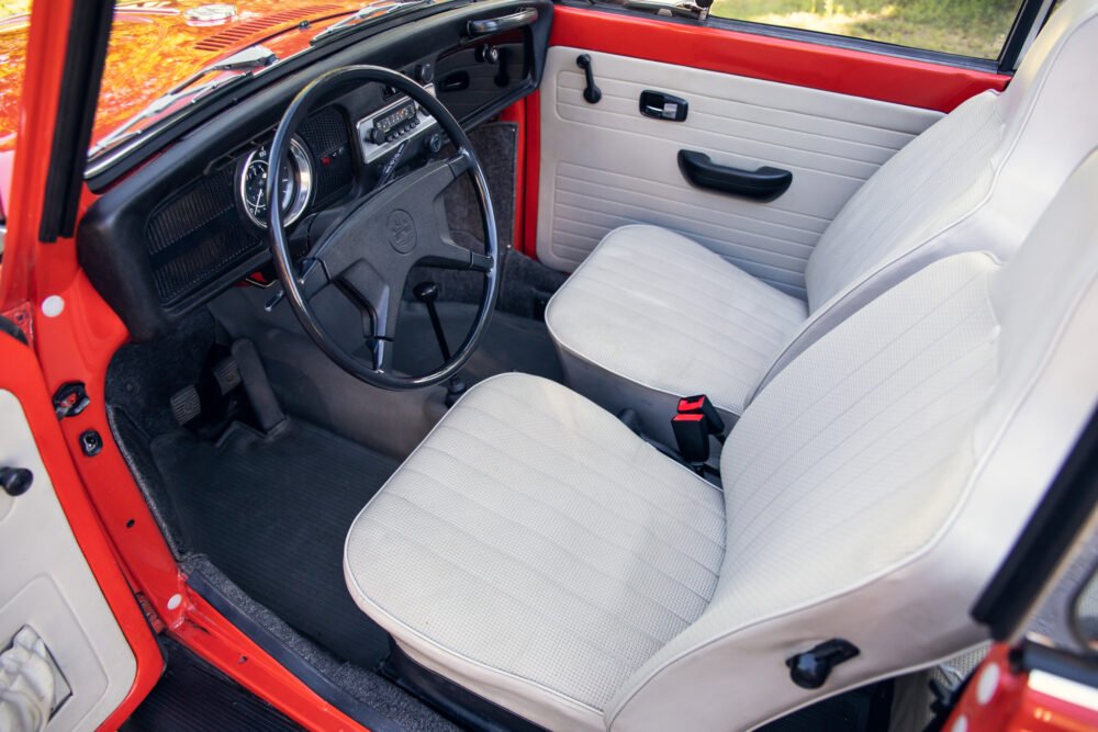 Vintage red car interior with white seats and dashboard.