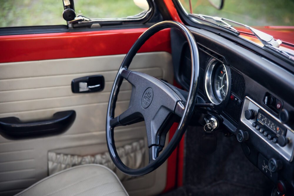 Vintage car interior with red dashboard and classic steering wheel.