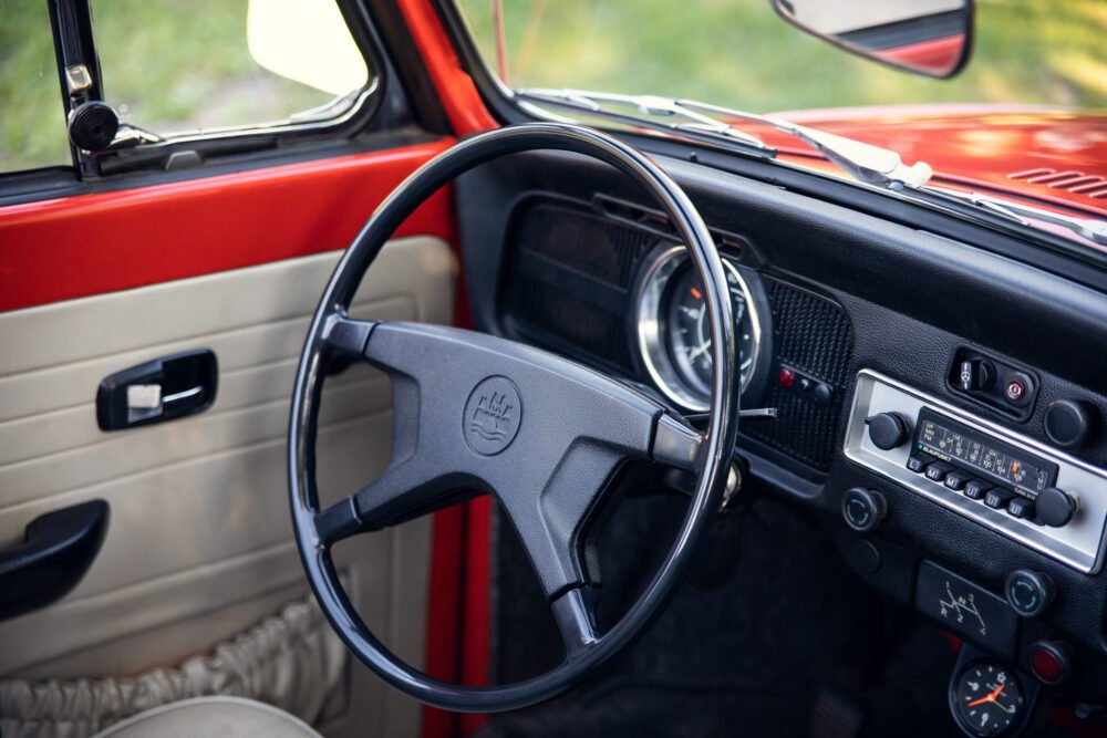 Vintage car interior with red dashboard and steering wheel.