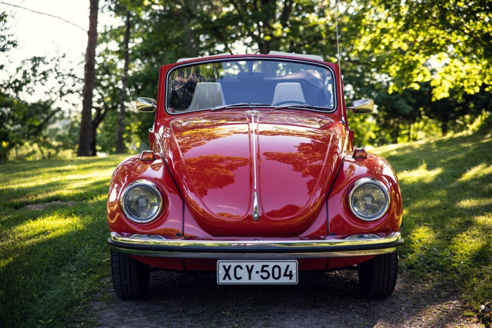 Red vintage Volkswagen Beetle parked in sunny green park.