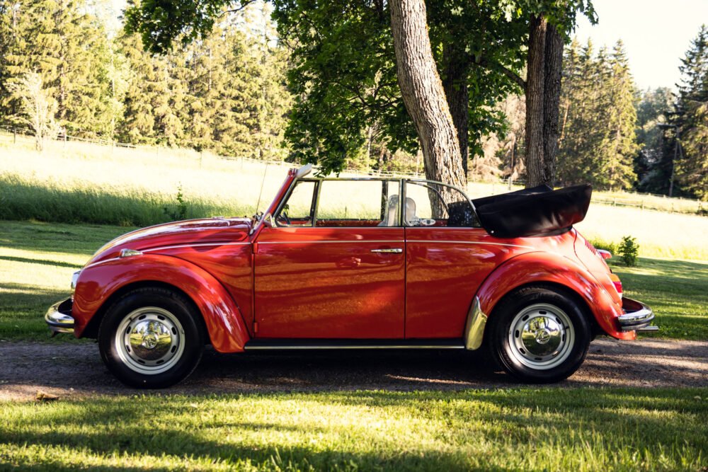 Red vintage convertible car parked under shady trees.