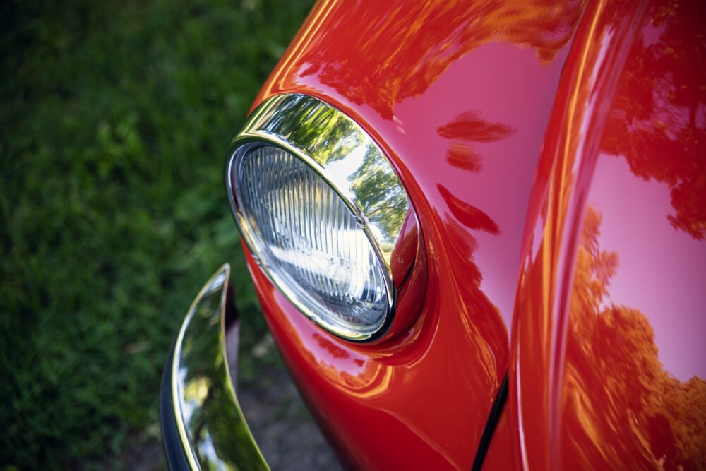 Close-up of vintage red car's headlight and chrome detailing.