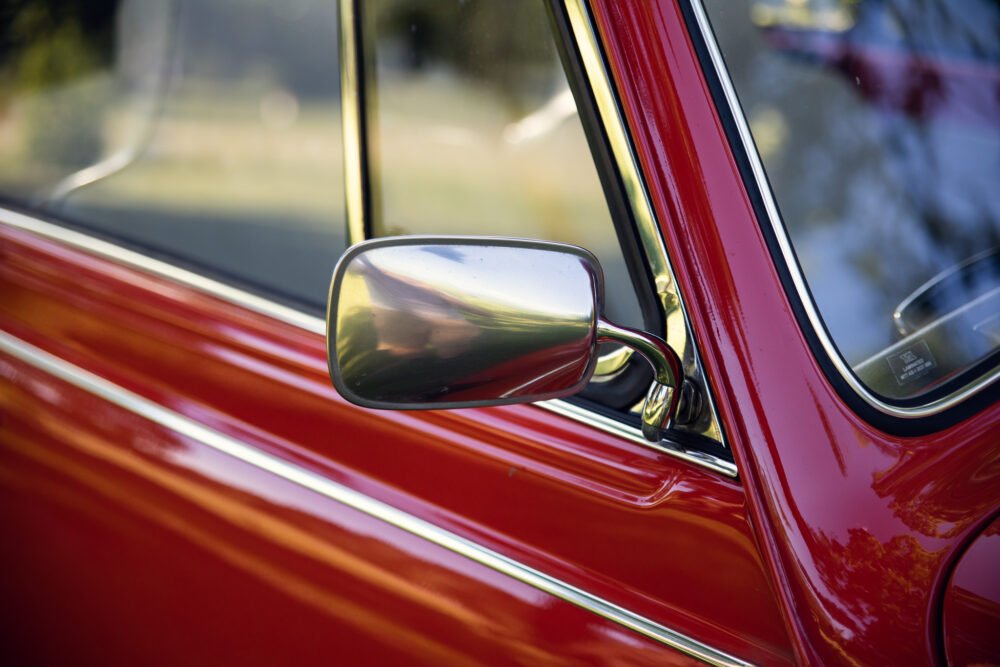 Vintage red car with chrome side mirror detail.