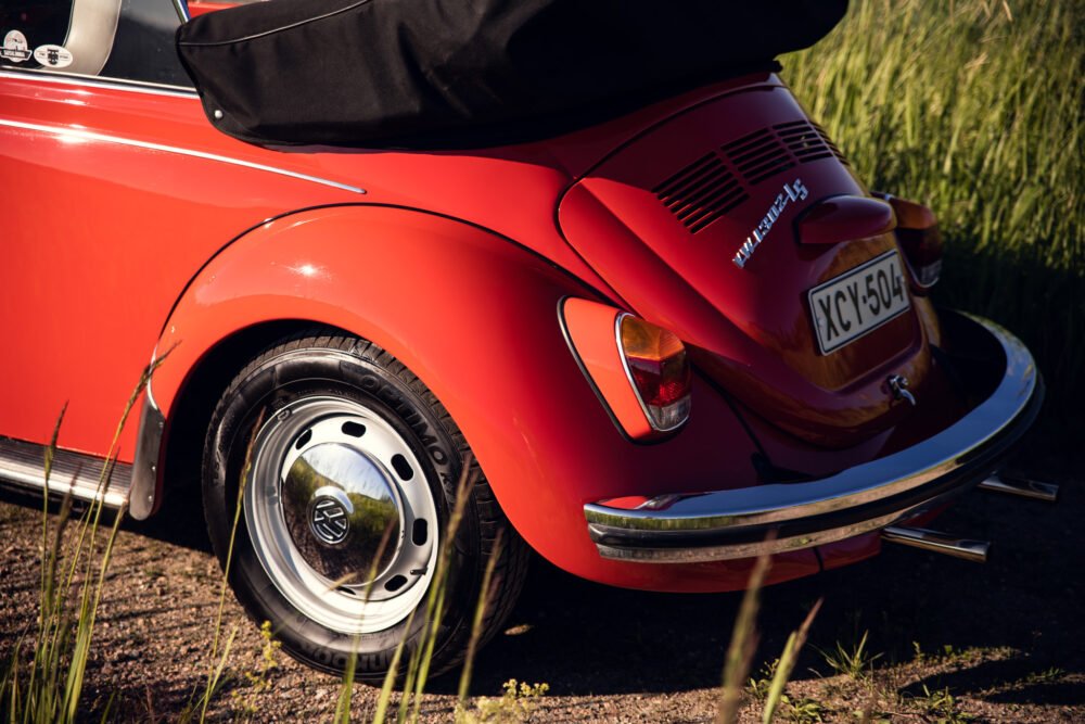 Red vintage Volkswagen Beetle parked in grassy field.