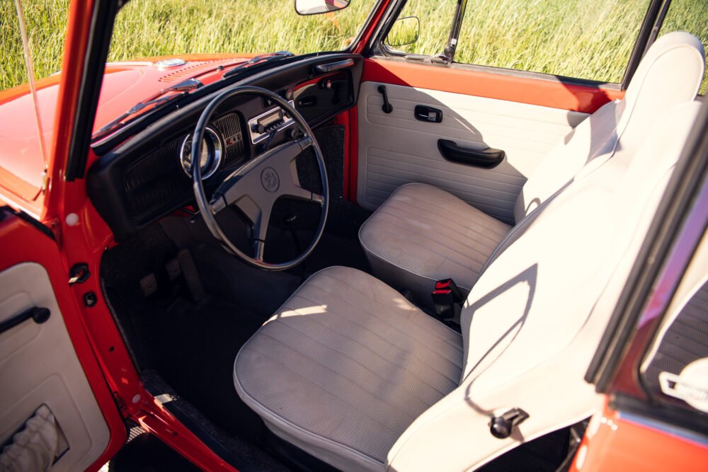 Vintage red car interior with open door in grassy field.
