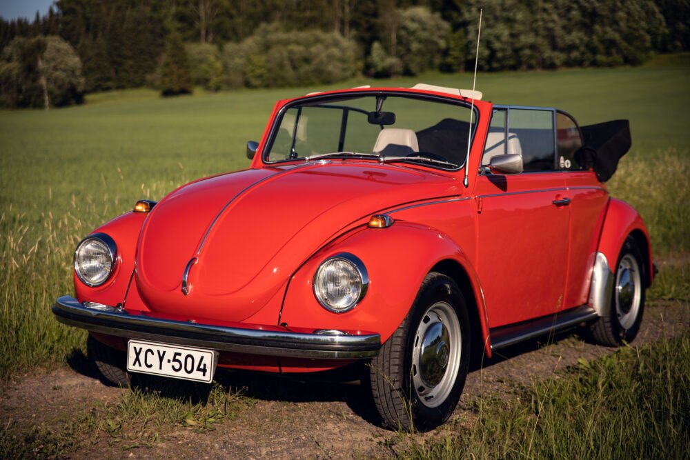 Red vintage convertible Beetle in sunny field.