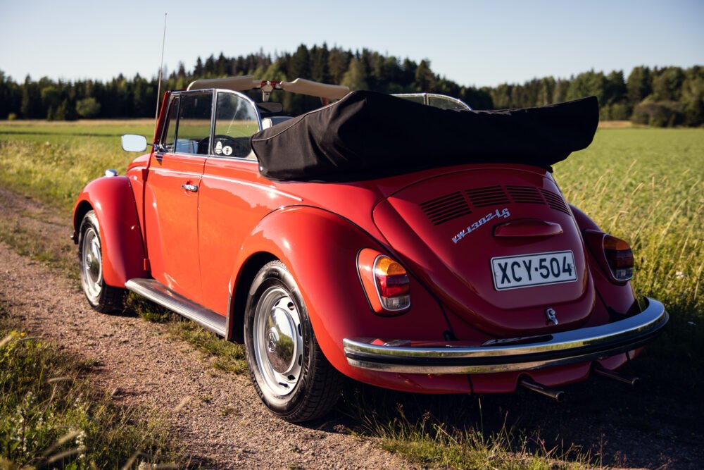 Red vintage convertible Beetle parked in countryside field.