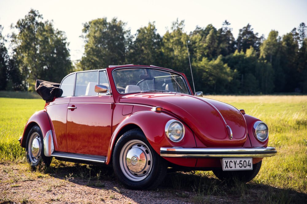 Red vintage convertible Volkswagen Beetle in sunny field.