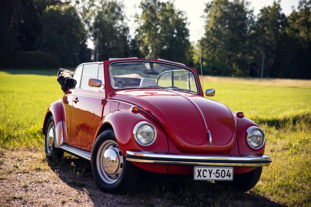 Vintage red Volkswagen Beetle convertible in sunny field.