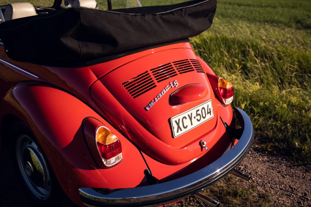 Red Volkswagen Beetle convertible parked on a grassy field.