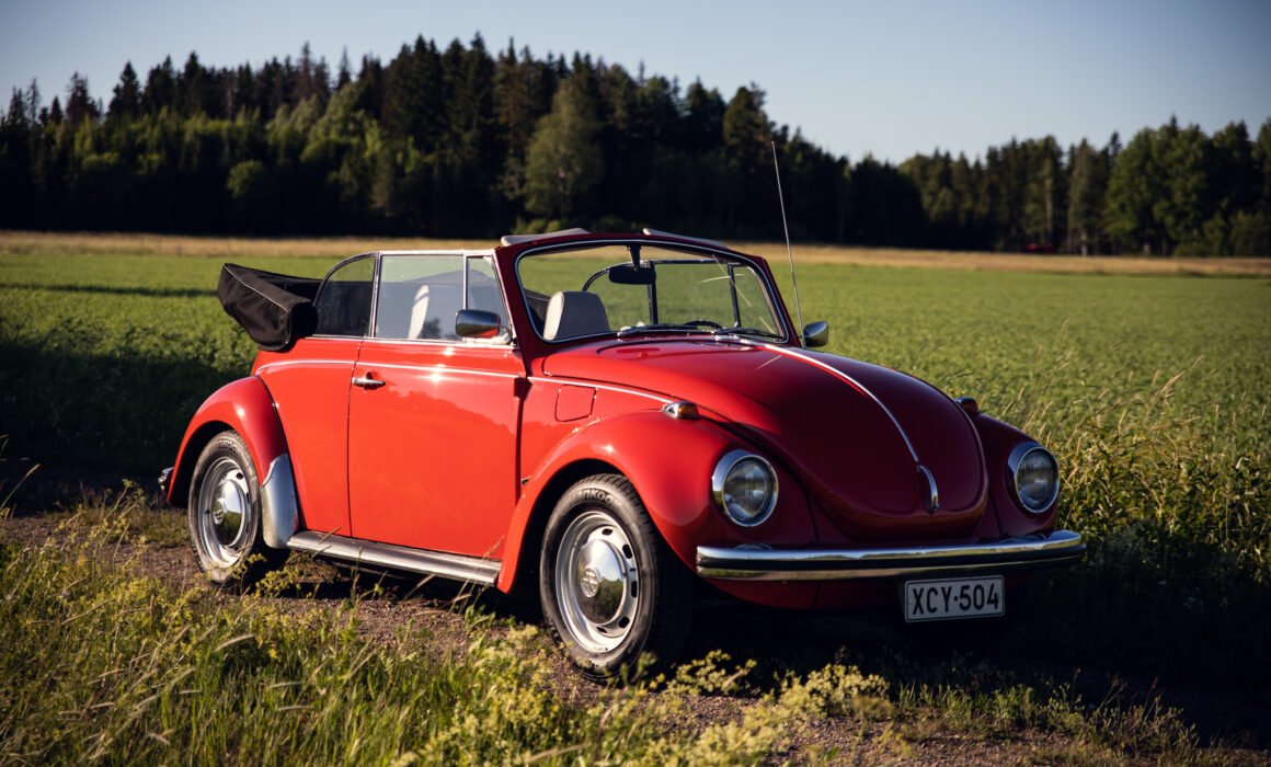 Red vintage convertible Beetle in a field.