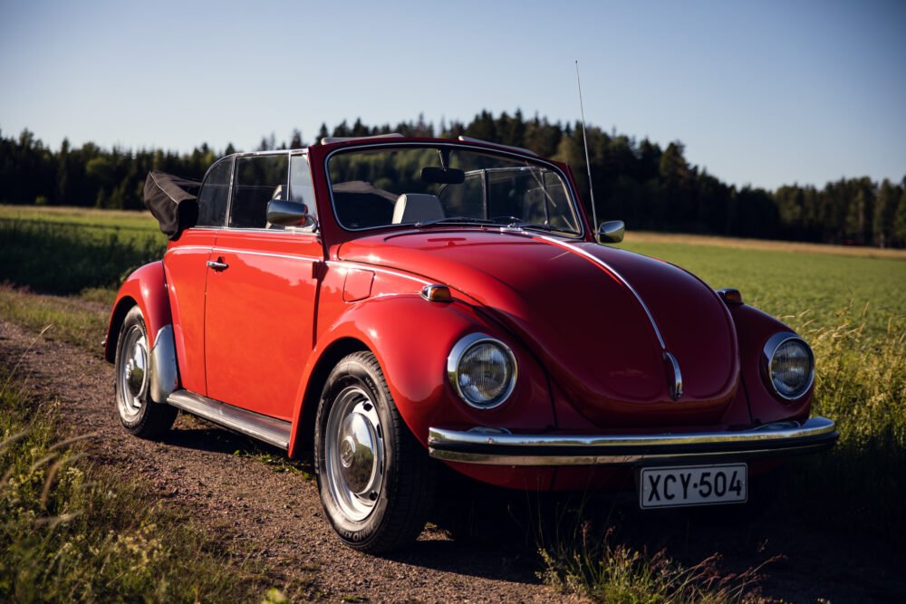 Red vintage convertible Beetle in sunny rural setting.