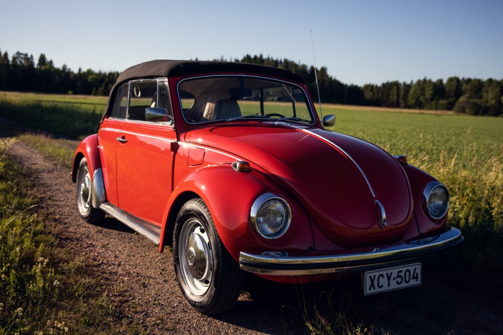 Red vintage convertible Beetle in countryside setting.