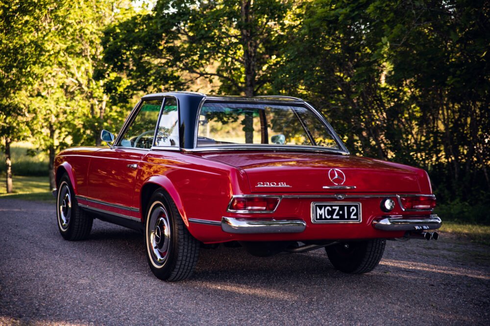 Vintage red Mercedes 230SL parked on tree-lined road.