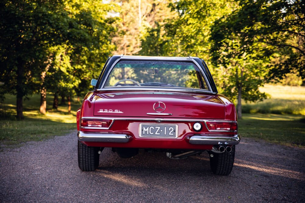 Red vintage Mercedes 280 SL on a forest-lined road.