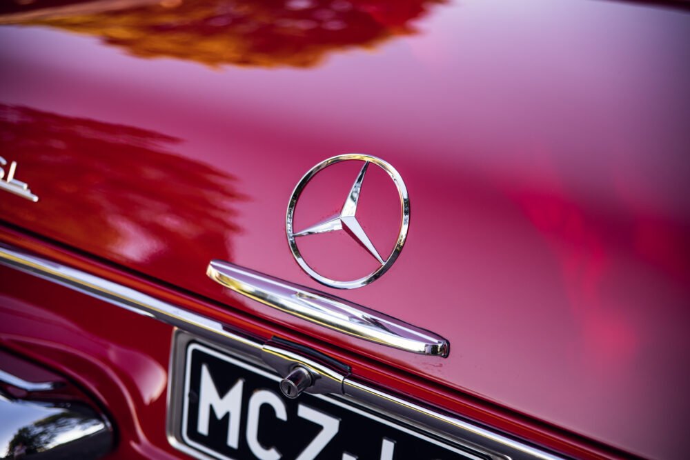 Mercedes emblem on red vintage car hood.