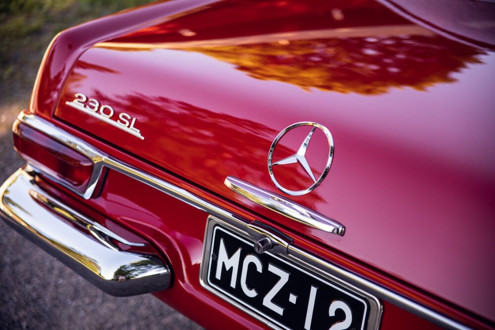 Red Mercedes 230SL, close-up on emblem and trunk.