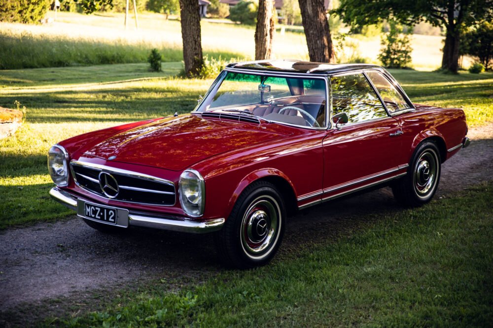 Vintage red Mercedes convertible parked in lush green park.