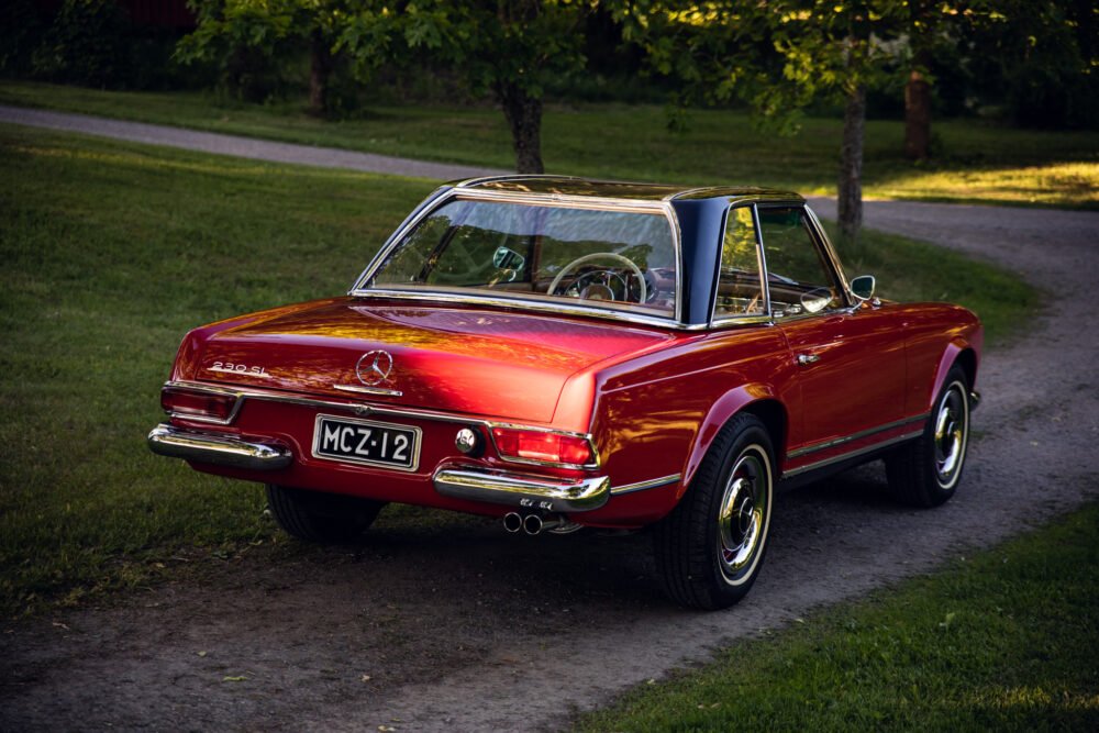 Vintage red Mercedes-Benz convertible in lush greenery.