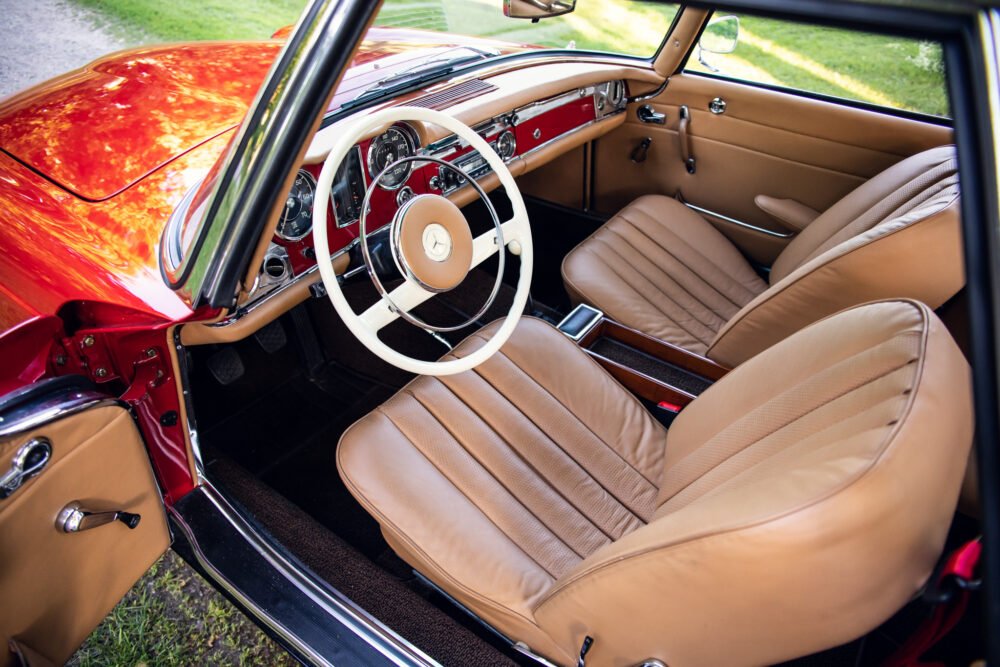Vintage Mercedes interior with red dashboard and tan seats.