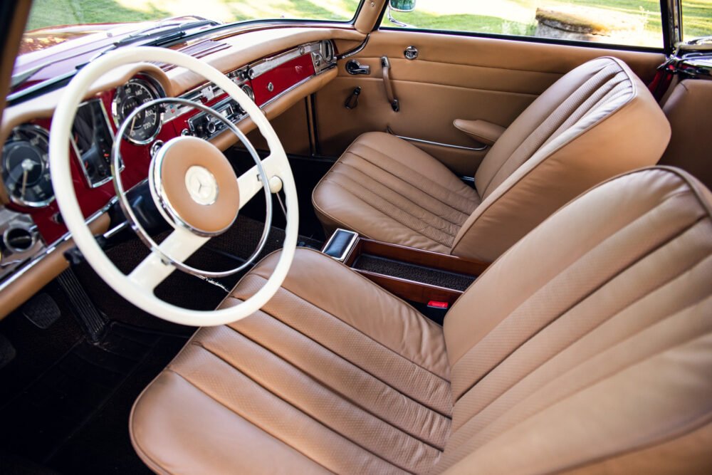 Vintage car interior with tan leather seats and red dashboard.