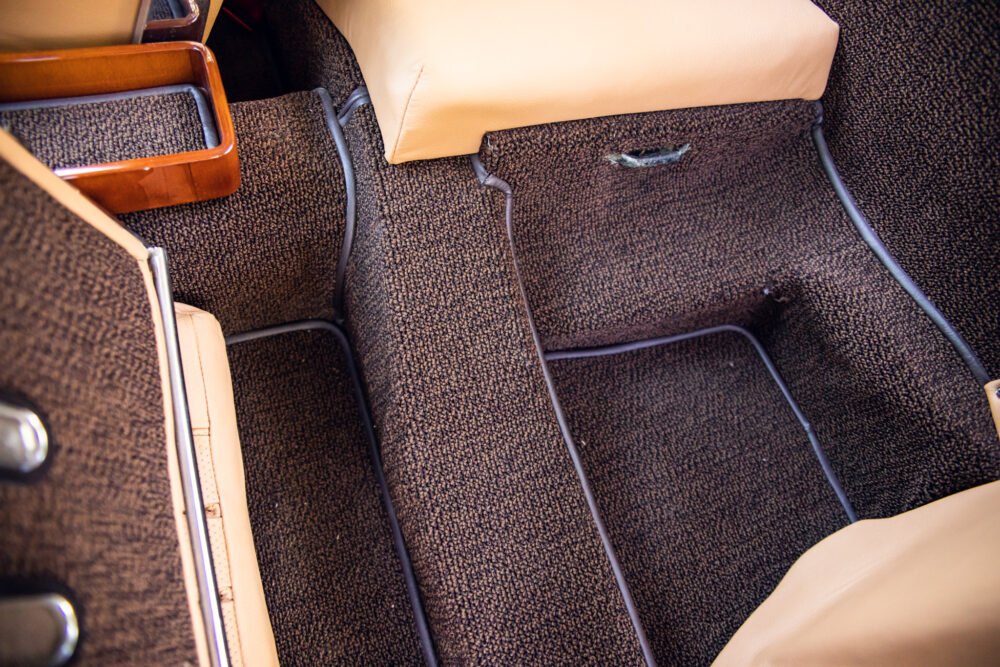 Vintage car interior with textured brown carpet and beige seats.