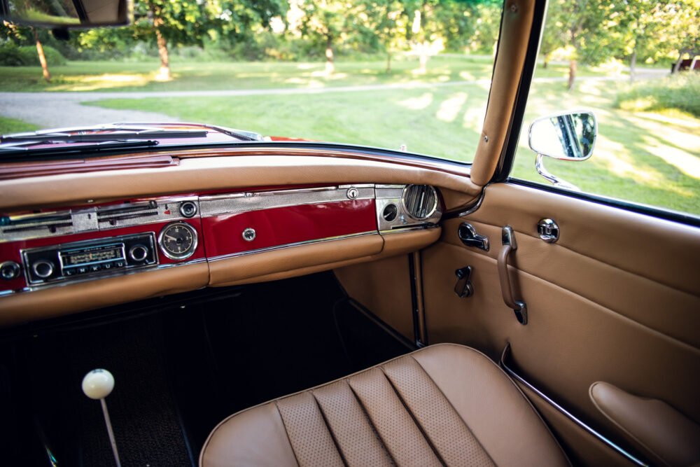 Vintage car interior with red dashboard and tan seats.