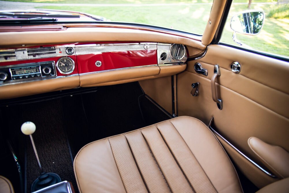 Vintage car interior with red dashboard and beige seats.