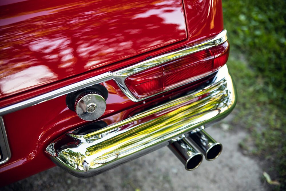 Close-up of shiny red vintage car's taillight and exhaust.