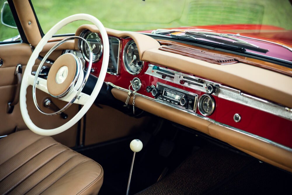Vintage car interior with white steering wheel and dashboard.