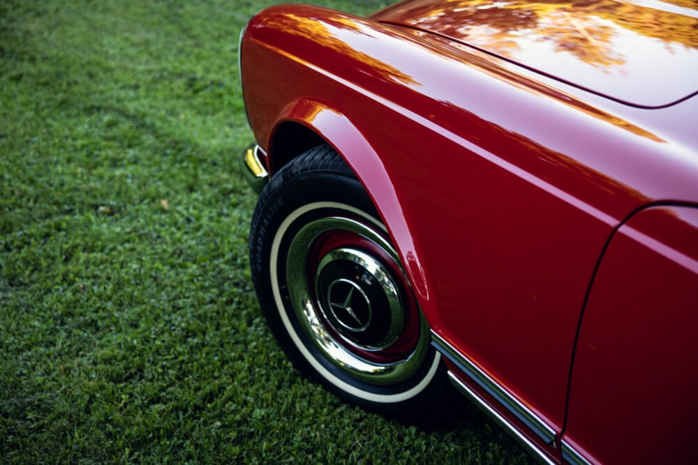 Red vintage car wheel and glossy fender on grass.
