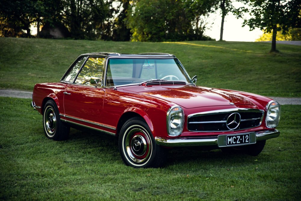 Vintage red Mercedes convertible parked on grass.