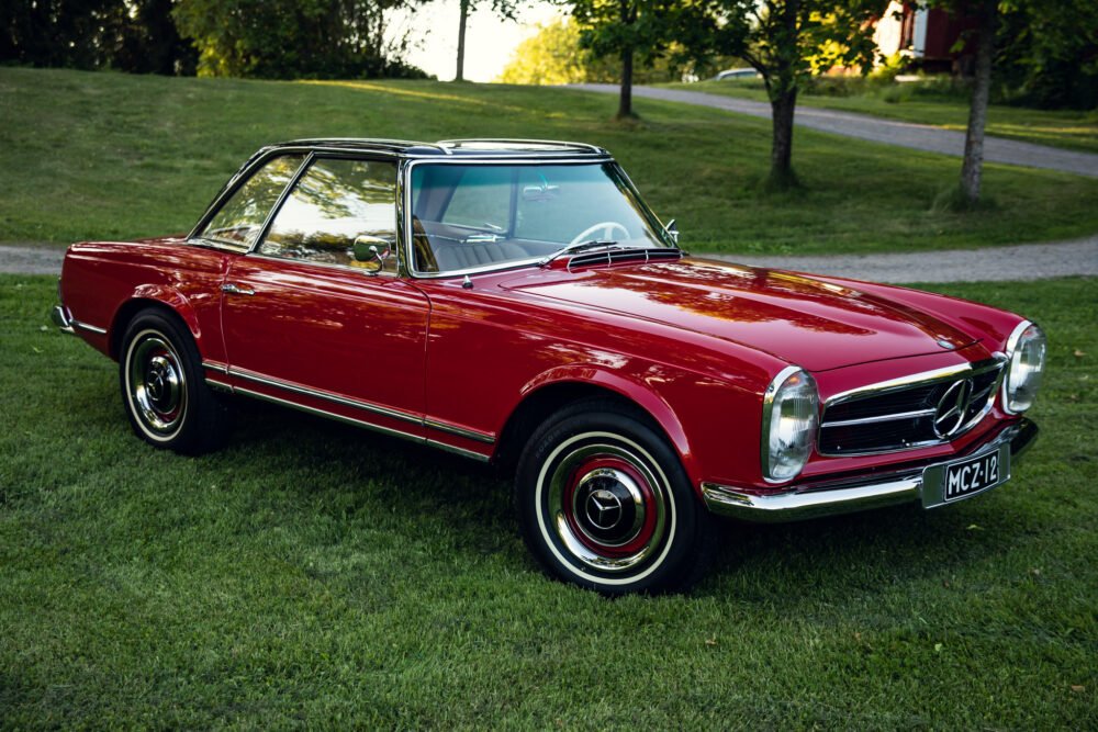 Vintage red Mercedes convertible on grassy background.