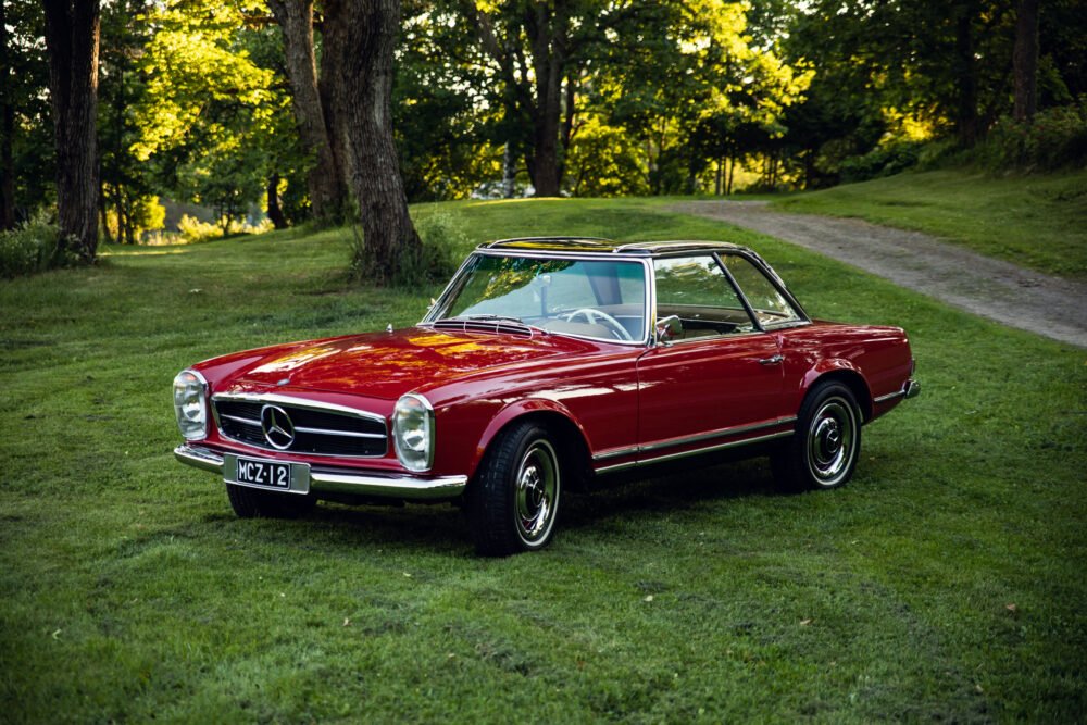 Vintage red Mercedes-Benz parked in lush green park.