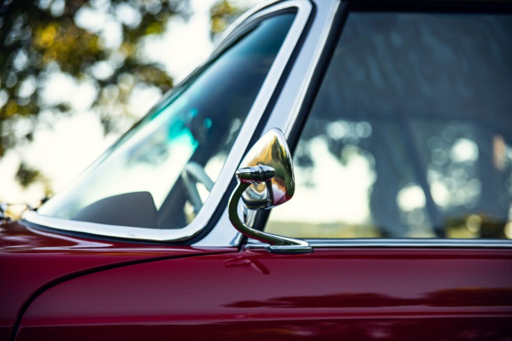 Close-up of vintage car's side mirror on red body.