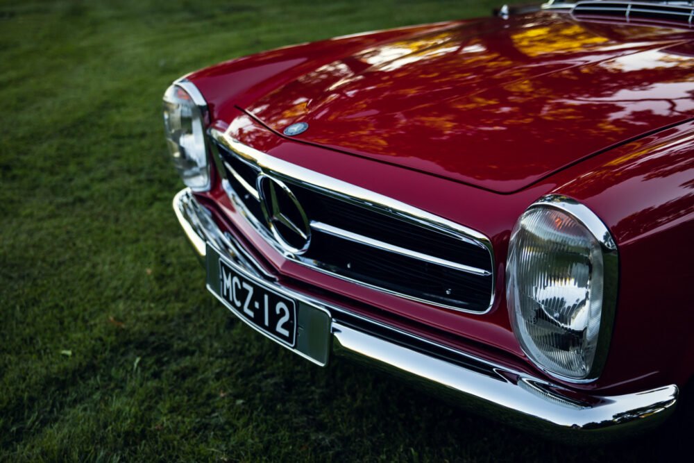Red vintage Mercedes-Benz on grass, close-up front view.