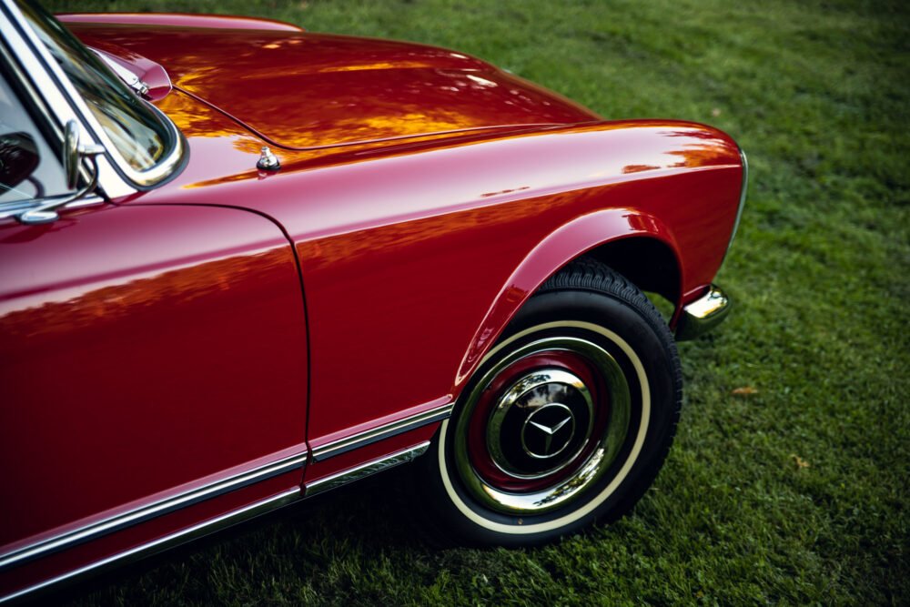 Red vintage car on grass, close-up of side and wheel.