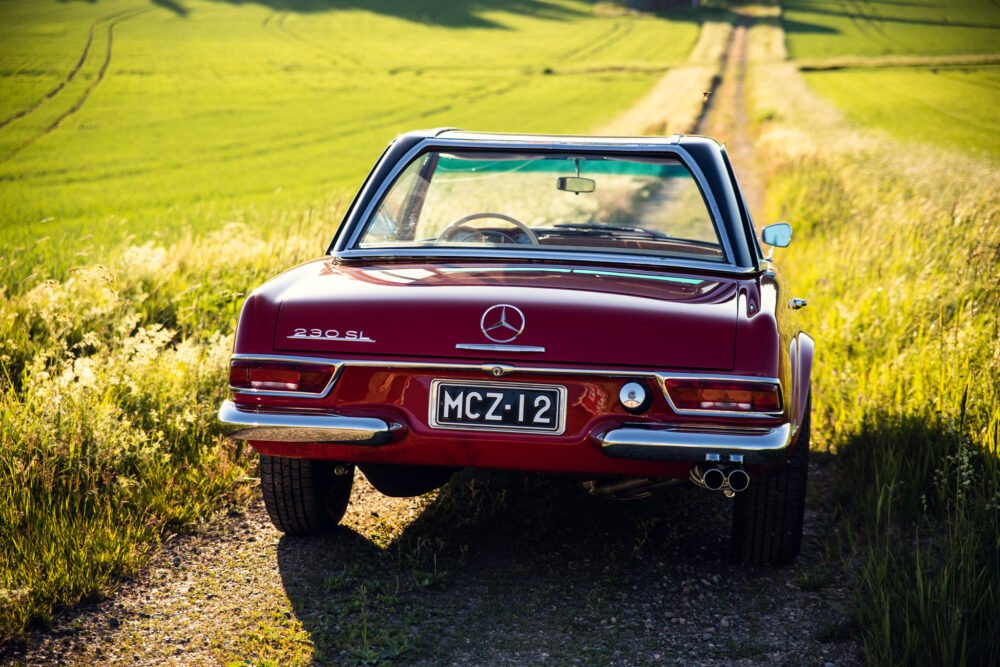 Red Mercedes 230 SL on rural road at sunset.